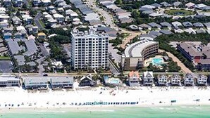 Vista aérea de uma área residencial costeira com um grande hotel, piscina e uma praia ao primeiro plano.