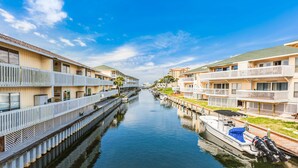 A canal with a boat docked on the right, surrounded by multi-story buildings with balconies and a clear sky. - Classic Florida condo near the beach with heated pool, hot tub, tennis, golf (Destin)