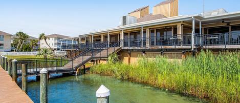 A waterfront hotel with a wooden deck, a bridge, and a grassy area.