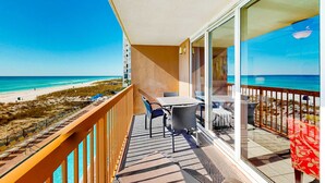 Un balcon avec une table et des chaises donnant sur une plage.