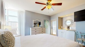 Een slaapkamer met een groot bed, een plafondventilator, een dressoir, een spiegel, een televisie en een raam met gordijnen.