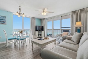 A living room with a sofa, a dining table with chairs, a TV, and a balcony with curtains.