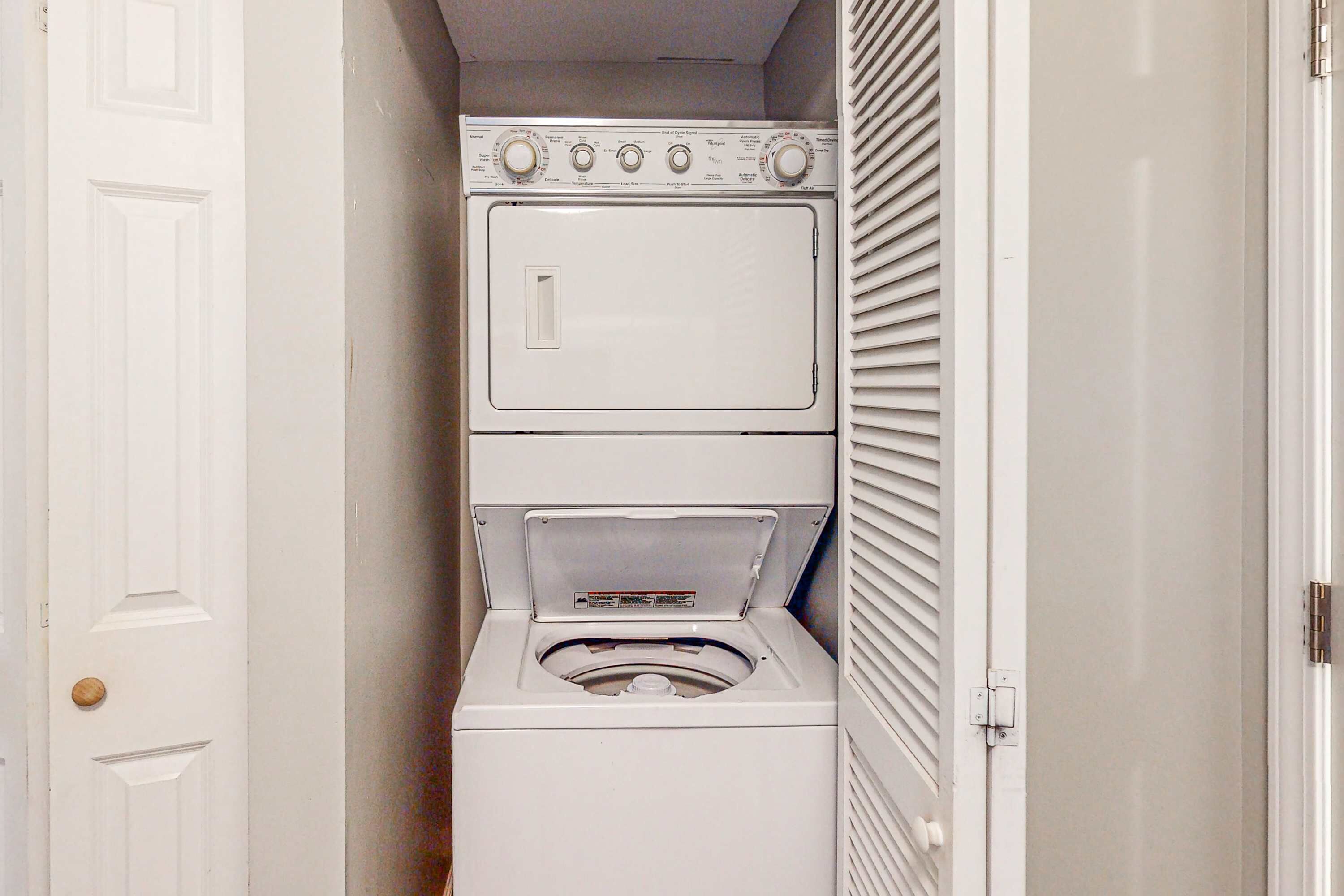 Uma lavanderia compacta com máquina de lavar e secadora empilhadas, uma porta e parede com ventilação.