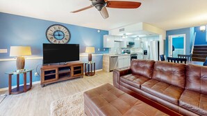 A living room with a brown leather sofa, a television, a wooden entertainment unit, and a ceiling fan. - Inviting townhouse with on-site pool, updated interior, & W/D (St. George Island)