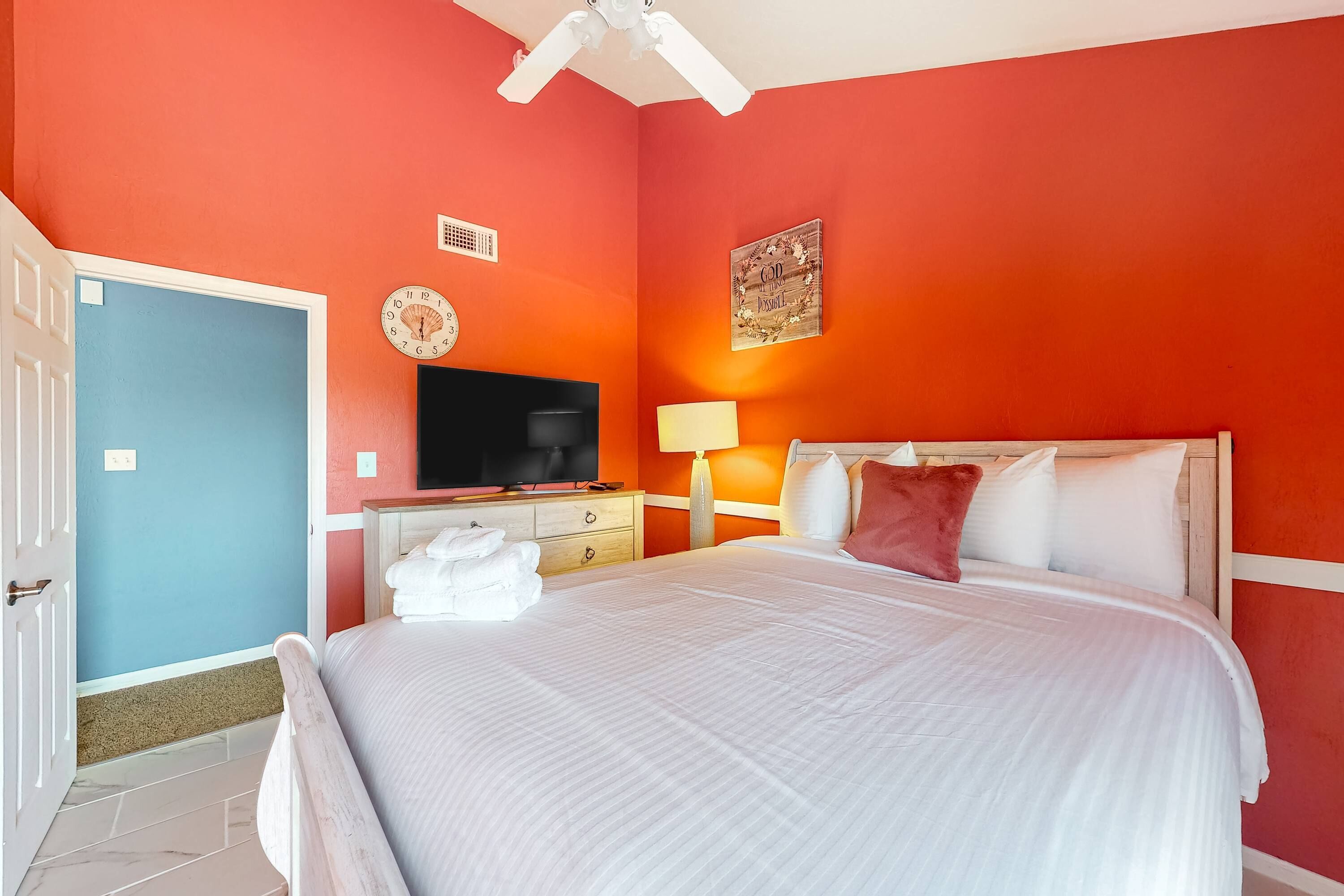 Quarto de hotel com uma cama grande, televisão, escrivaninha com abajur e porta.