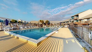 A swimming pool with lounge chairs and umbrellas, surrounded by wooden deck and buildings with balconies. - Inviting townhouse with on-site pool, updated interior, & W/D (St. George Island)
