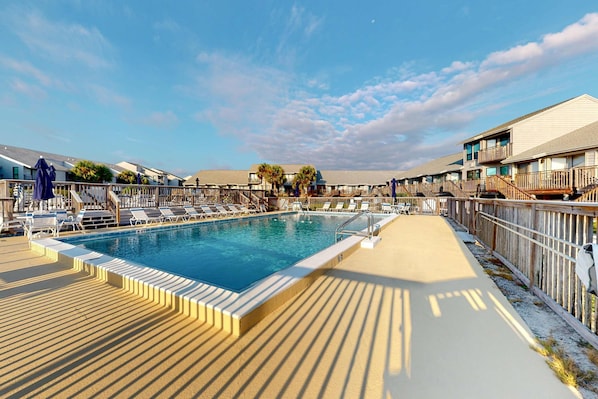 A swimming pool with lounge chairs and umbrellas, surrounded by wooden deck and buildings with balconies. - Inviting townhouse with on-site pool, updated interior, & W/D (St. George Island)