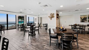 Une salle à manger spacieuse avec de grandes fenêtres donnant sur l’océan, un plancher en bois et un mobilier moderne.