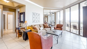 Un vaste espace de vie comprenant un canapé, un fauteuil et une table basse. On y trouve également un coin repas avec une table et des chaises, ainsi que de grandes fenêtres offrant une vue dégagée.