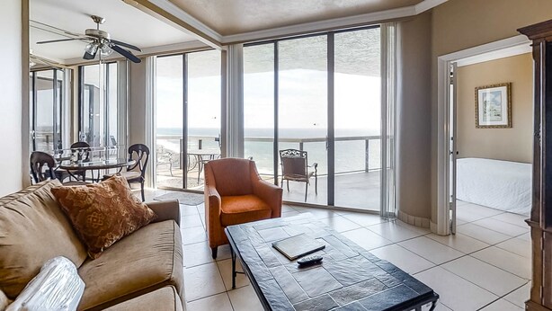 Un vaste espace de vie doté d’une grande porte-fenêtre coulissante donnant sur un balcon, d’un ventilateur de plafond et d’un coin repas visible à travers la vitre.