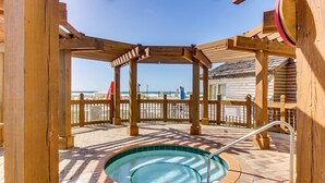Un belvédère en bois avec un jacuzzi, une clôture en bois et une vue sur la plage.