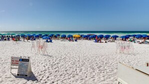 Une plage de sable blanc avec des parasols bleus. Un panneau est visible au premier plan.