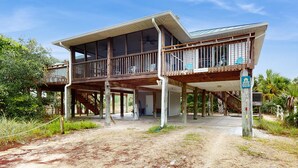 A two-story wooden house with a balcony, a covered porch, and a dirt driveway. - Dog-friendly home near the beach with spacious living area, porch & sundeck (Port St. Joe)