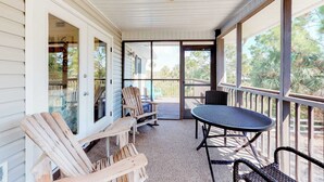 A covered porch with wooden chairs and a table, large windows, and a view of the outdoors. - Dog-friendly home near the beach with spacious living area, porch & sundeck (Port St. Joe)