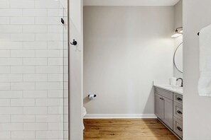 A bathroom with white tiled walls, a wooden floor, a sink with a mirror, and a towel hanging on the wall. - Dog-friendly bay view duplex with full kitchen, washer/dryer, & central AC (Port St. Joe)