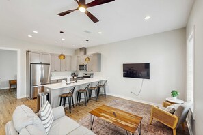 A modern kitchen with stainless steel appliances, a central island with bar stools, and a dining area with a wooden table and chairs. - Dog-friendly bay view duplex with full kitchen, washer/dryer, & central AC (Port St. Joe)