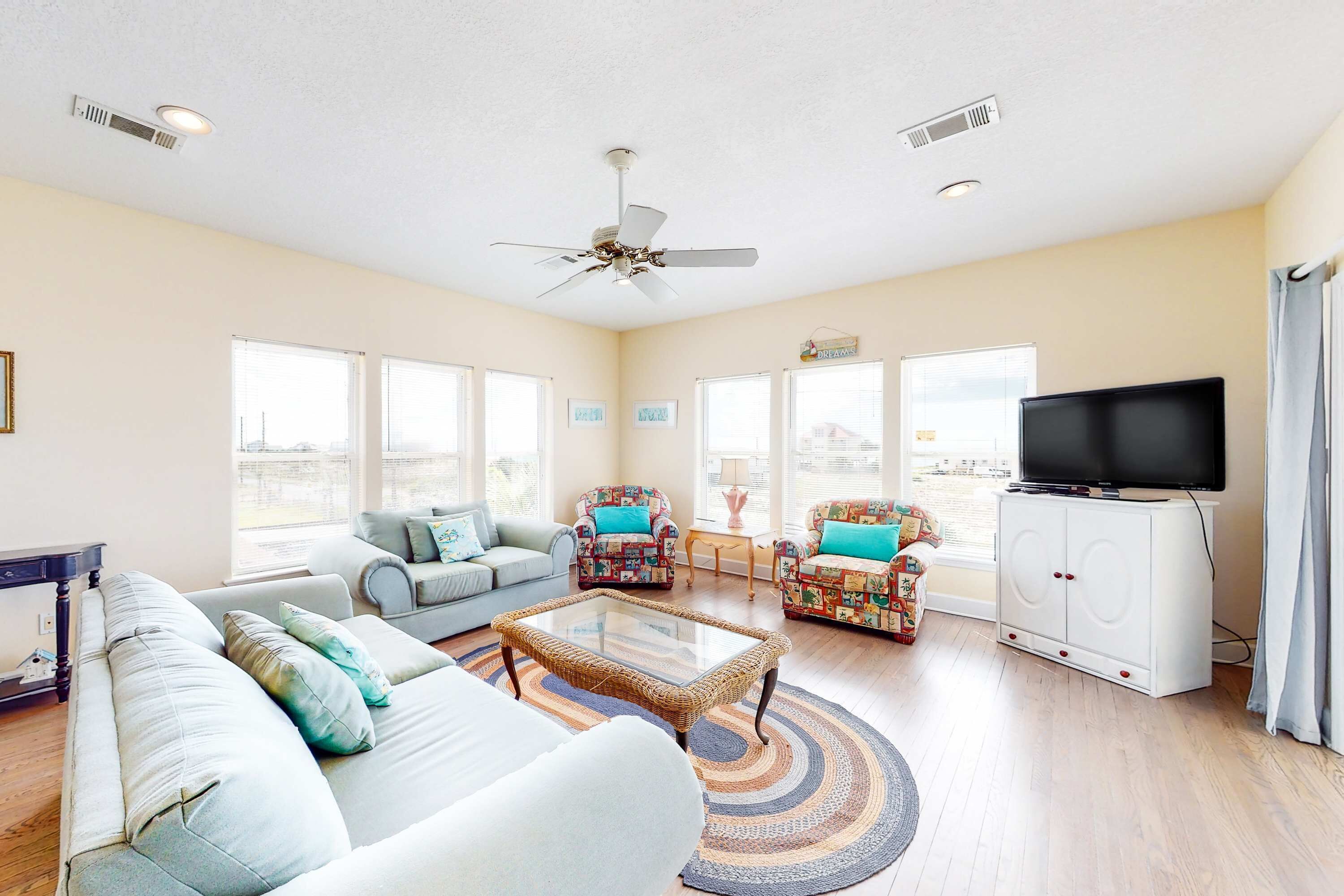 A spacious living room with a large sofa, two armchairs, a coffee table, a television, and a ceiling fan.