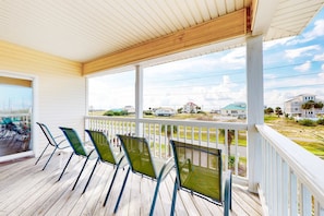 A covered porch with four green chairs and a view of a residential area. - Charming ocean-view gem with a pool, deck, washer/dryer & central AC (St. George Island)