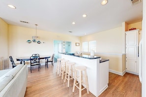 A kitchen with a central island, wooden flooring, and white cabinetry. - Charming ocean-view gem with a pool, deck, washer/dryer & central AC (St. George Island)