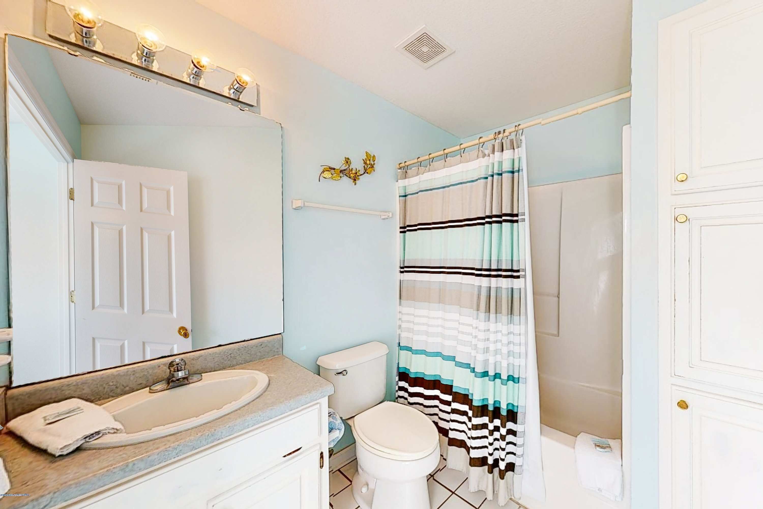 A bathroom with a white sink, a toilet, a shower curtain, and a mirror with lights.