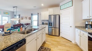 A modern kitchen with white cabinets, a stainless steel refrigerator, granite countertops, and a chandelier. - Dog friendly home and casita with pool plus beach access, central AC, and laundry (Port St. Joe)