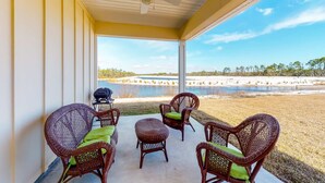 A covered patio with wicker furniture and a ceiling fan, overlooking a beach and water. - Dog friendly home and casita with pool plus beach access, central AC, and laundry (Port St. Joe)