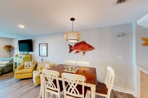 Un coin repas avec une table en bois, des chaises blanches, une décoration murale représentant des poissons et un luminaire suspendu.