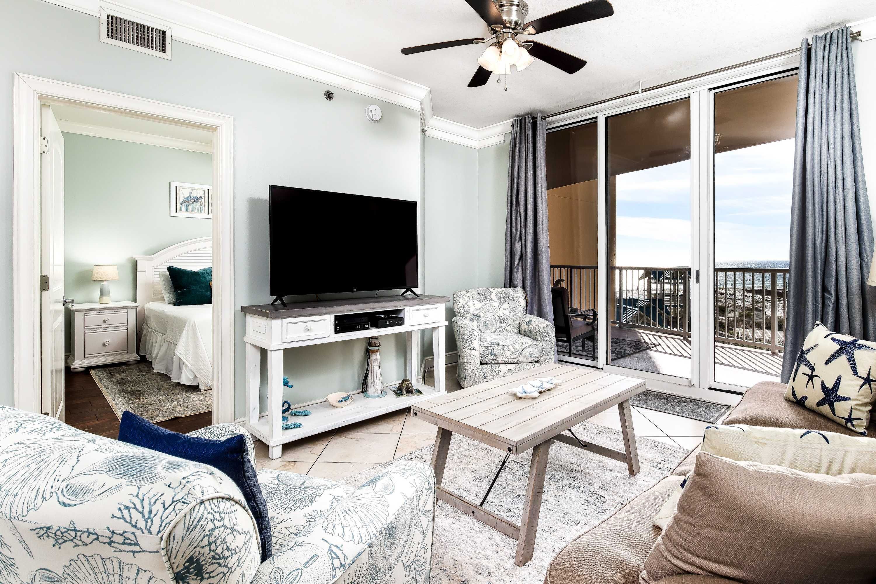 Habitación de hotel con televisor, sofá, silla, mesa y balcón con vistas.