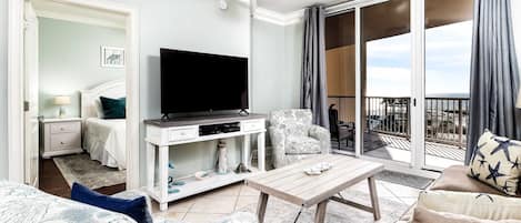 Habitación de hotel con televisor, sofá, silla, mesa y balcón con vistas.