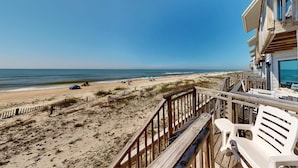Une vue sur la plage depuis un balcon doté d’une terrasse en bois, de chaises de plage et d’une plage de sable avec des parasols.