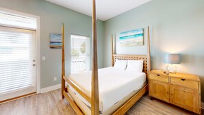A four-poster bed with a wooden headboard, a nightstand with a lamp, and a painting on the wall. - Dog-friendly home near beach with pool, four balconies, WD & AC (Panama City Beach)
