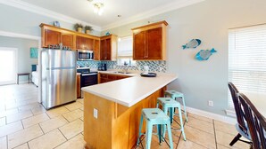 A kitchen with wooden cabinets, a stainless steel refrigerator, a large island with stools, and a backsplash with blue tiles. - Dog-friendly home near beach with pool, four balconies, WD & AC (Panama City Beach)