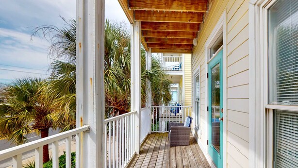 A wooden deck with a railing, a wicker chair, and a door with a window. - Dog-friendly home near beach with pool, four balconies, WD & AC (Panama City Beach)