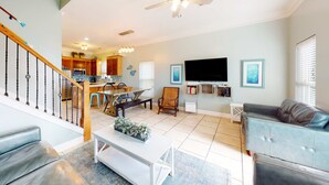 A spacious living room with a sofa, a coffee table, a TV, and a staircase leading to a kitchen. - Dog-friendly home near beach with pool, four balconies, WD & AC (Panama City Beach)