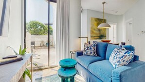 A modern living room with a blue sofa, a round coffee table, and a large window with curtains. - Cozy ground-floor condo with private patio, shared pool & beach access (Miramar Beach)