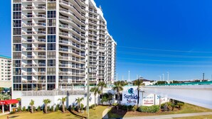 A high-rise hotel with multiple balconies, a sign for Surfside Resort, and a clear blue sky. - Cozy ground-floor condo with private patio, shared pool & beach access (Miramar Beach)