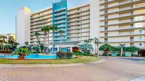 Ein mehrstöckiges Hotel mit einer auffälligen Schilder, auf denen "Sterling Shores" steht. Es verfügt über einen zentralen Innenhof mit einem Pool, der von Palmen und Grünpflanzen umgeben ist.