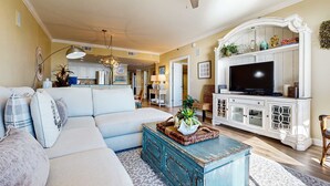 A living room with a sofa, coffee table, and TV stand. - Ocean view condo with pool, gym, grill, scenic balcony, open layout, W&D, & AC (Destin)