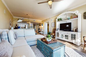 A living room with a sofa, coffee table, and TV stand. - Ocean view condo with pool, gym, grill, scenic balcony, open layout, W&D, & AC (Destin)