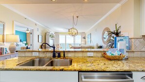 A kitchen with granite countertops, stainless steel sink, and modern appliances. - Ocean view condo with pool, gym, grill, scenic balcony, open layout, W&D, & AC (Destin)