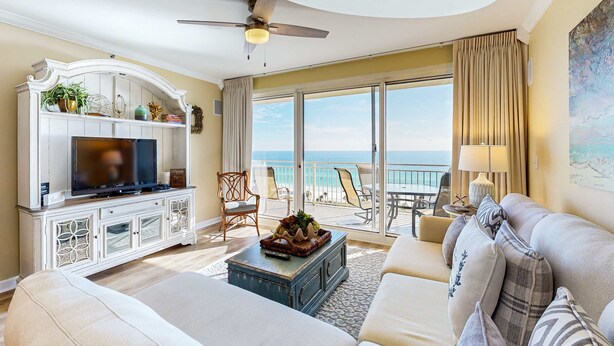 A spacious living room with a television, a sofa, a coffee table, and a balcony with a view of the ocean. - Ocean view condo with pool, gym, grill, scenic balcony, open layout, W&D, & AC (Destin)
