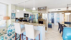 Een moderne keuken met een centraal eiland, barkrukken en een eethoek met rieten stoelen.