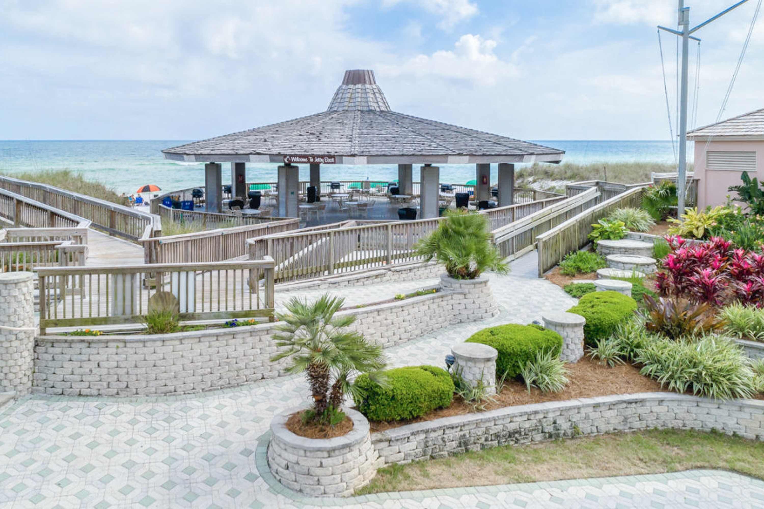 A beachside gazebo with a tiled patio, surrounded by stone walls and landscaped gardens.