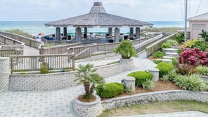 Een tuinhuis aan het strand met een betegeld terras, omgeven door stenen muren en aangelegde tuinen.
