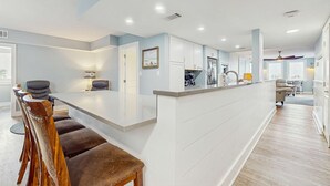 Een moderne keuken met witte kasten, een centraal eiland en een eethoek met houten stoelen.