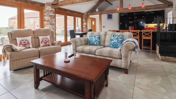 A spacious living room with a wooden coffee table, two sofas with floral cushions, and a kitchen in the background. - Pillar Barn (Driffield)