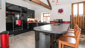 A modern kitchen with a central island, black appliances, and wooden beams. - Pillar Barn (Driffield)