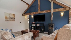 A living room with a high ceiling, exposed wooden beams, a fireplace, a television, and a painting on the wall. - Pillar Barn (Driffield)