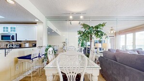 Una cocina moderna con armarios blancos, microondas y un comedor con mesa de vidrio y sillas blancas.