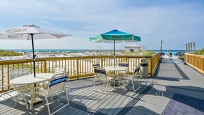 Un terrazzo in legno con posti a sedere all'aperto, vista sulla spiaggia e una torretta di salvataggio sullo sfondo.